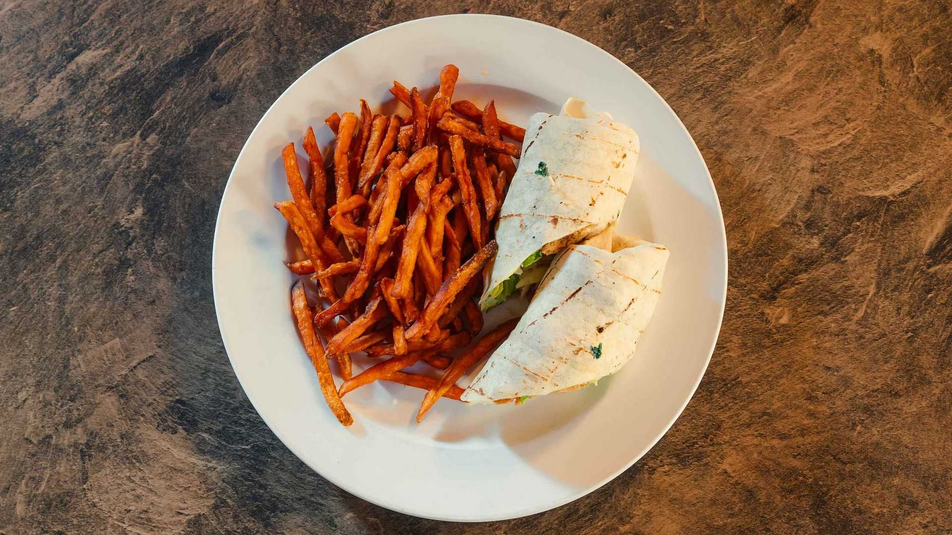 Plate with a wrap sandwich and crispy fries on a rustic wooden table.