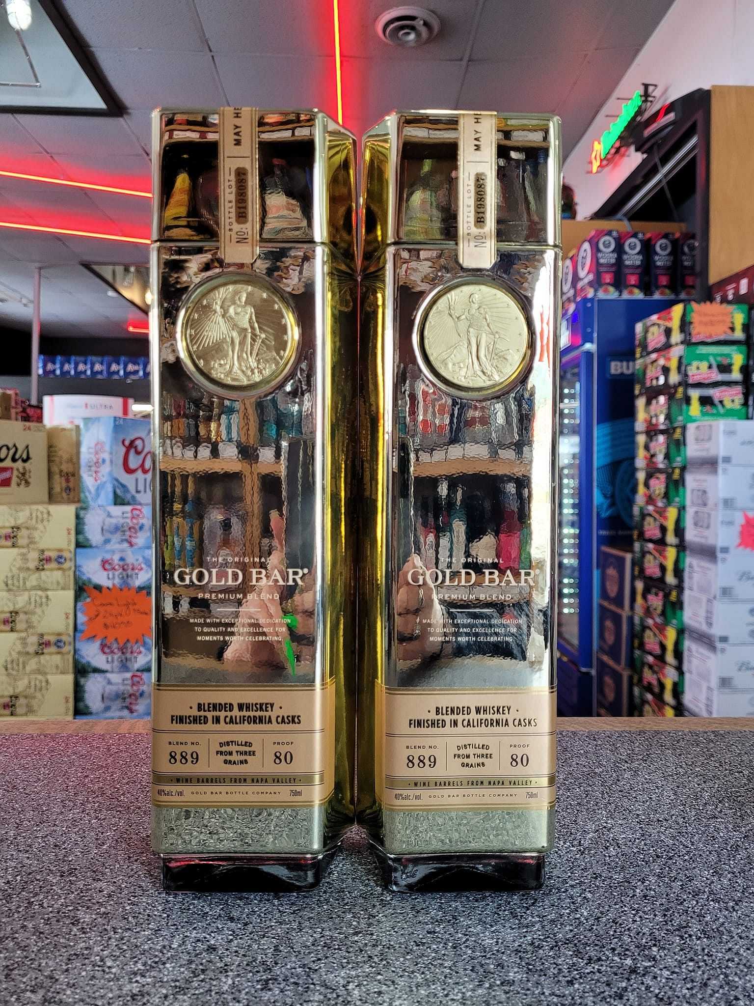 Two bottles of Gold Bar whiskey on a store counter with various beverages in the background.