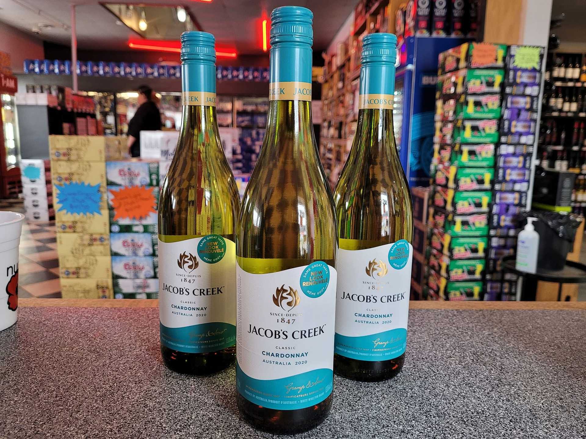 Three bottles of Jacob's Creek Chardonnay on a store counter with various products in the background.