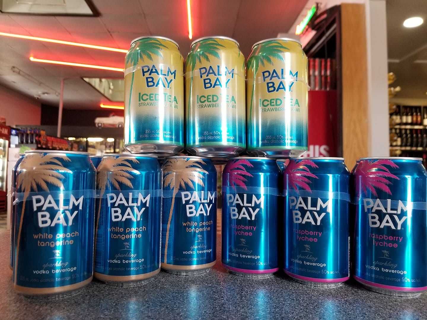 Cans of Palm Bay beverages in different flavors stacked on a countertop in a store.